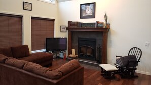 Una sala de estar con chimenea, un sofá de cuero marrón, una televisión y una estantería.