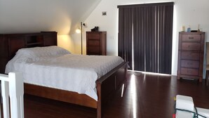 Un dormitorio con una cama de madera, un ventilador de techo, un aparador y una ventana con cortinas.
