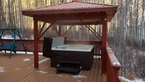 Una terraza de madera con un jacuzzi, un columpio y una pérgola.