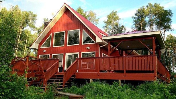 Una cabaña roja de madera con balcón, rodeada de follaje.