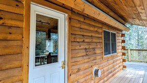 Une cabane en bois avec une porte blanche, une fenêtre et une petite terrasse extérieure.