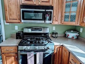 A kitchen with wooden cabinets, a stainless steel stove, a microwave, and a slow cooker. - Woodland House w/ Deck, Near Beaches & Acadia (Hancock)