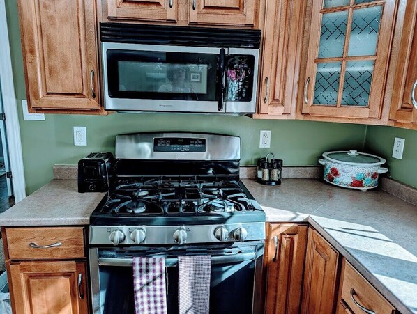 A kitchen with wooden cabinets, a microwave, a stove, and a slow cooker.