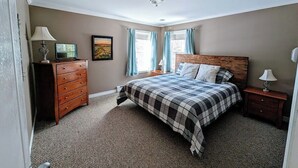 Een slaapkamer met een bed, een dressoir, een nachtkastje en een raam met gordijnen.