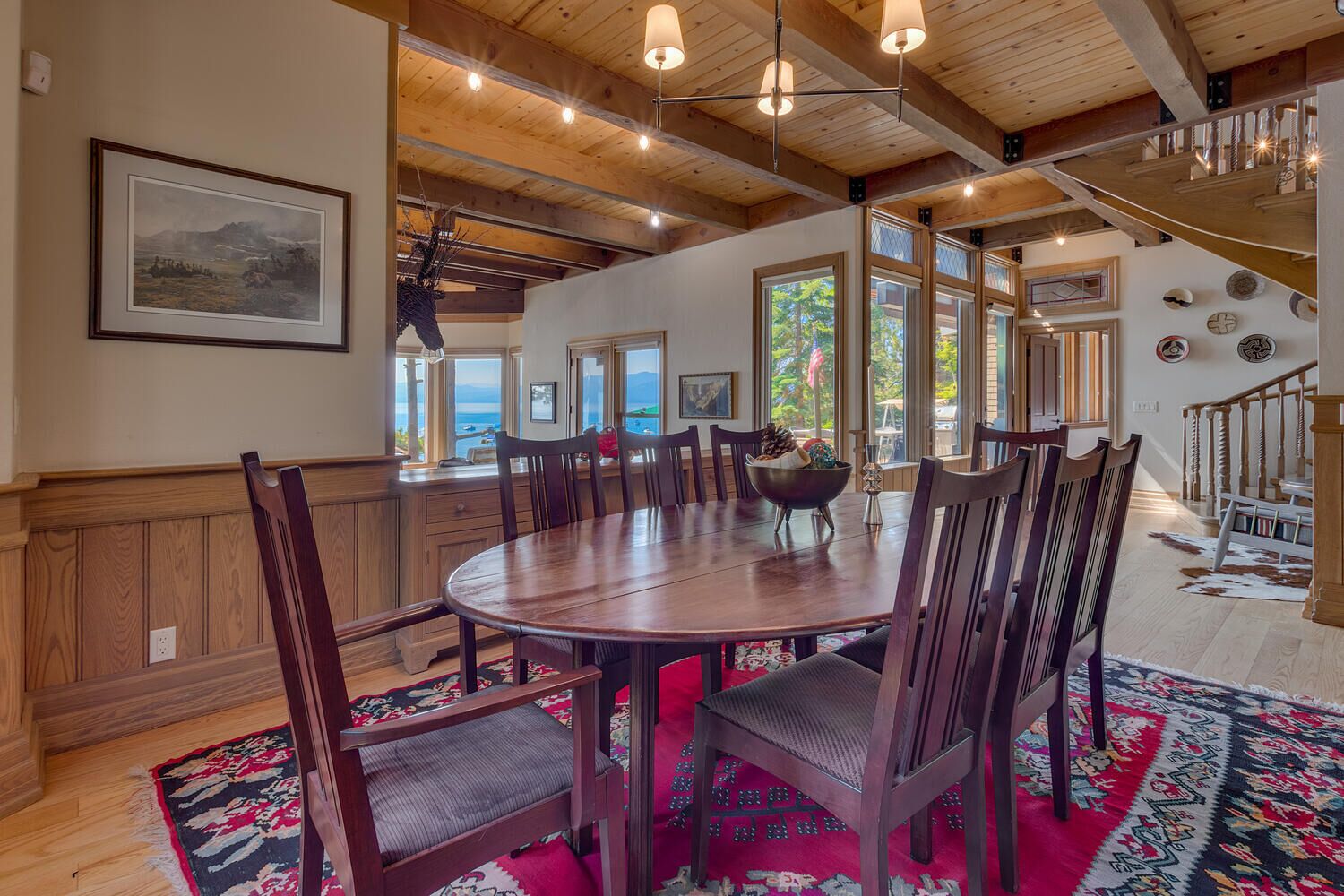 A spacious dining area with a large wooden table and chairs, surrounded by large windows offering views of the outdoors.