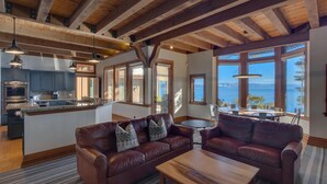 Un'ampia zona giorno con soffitto in legno, una cucina con piani di lavoro in granito e ampie finestre con vista sull'acqua.