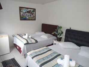 A hotel room with two beds, a small bedside table, a nightstand, a potted plant, and a painting on the wall. - Pousada Iza I (Guarujá)