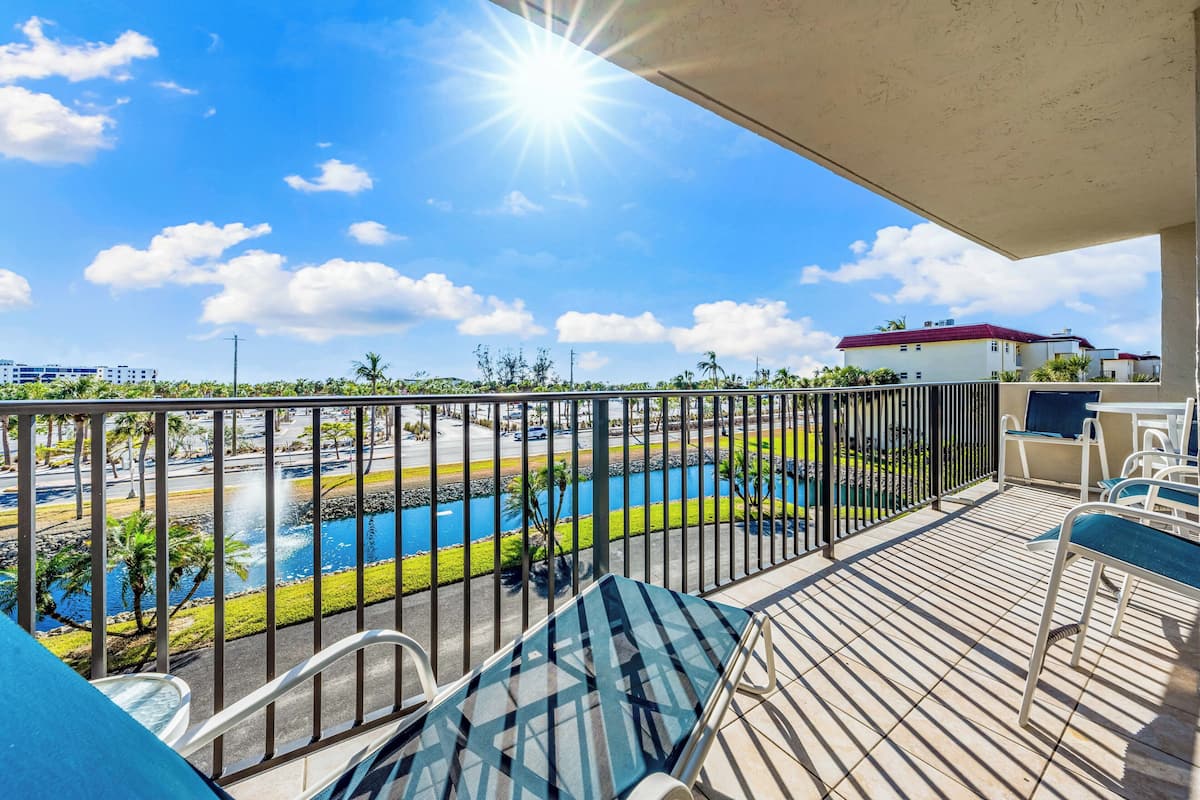 Un balcon donnant sur une piscine, un parking et un immeuble avec un toit rouge.