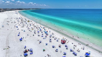 Une vaste plage parsemée de nombreux parasols et de chaises longues, une tour de surveillance pour les sauveteurs et une vue dégagée sur l’océan.