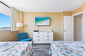 Une chambre d’hôtel avec deux lits, un téléviseur fixé au mur, une commode et une fenêtre avec des rideaux.