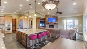 A spacious kitchen with a central island, bar stools, a stone fireplace, and a ceiling fan. - Luxury Private Estate | Pool & Pickleball Court (Lakeside)