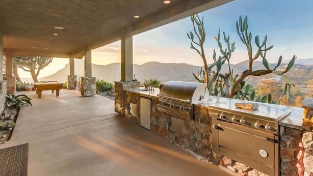 An outdoor kitchen with a stone wall, a grill, and a view of the mountains. - Luxury Private Estate | Pool & Pickleball Court (Lakeside)