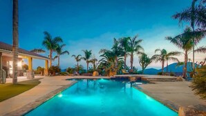 A rectangular swimming pool with clear blue water, surrounded by palm trees and a building with a tiled roof. - Luxury Private Estate | Pool & Pickleball Court (Lakeside)