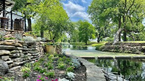 Un jardin paisible avec un bassin, des murs en pierre et une terrasse en bois.
