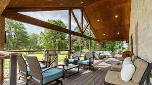 Un espace extérieur aménagé, abrité et doté de chaises et d’un canapé en osier, offrant une vue sur un paysage verdoyant.