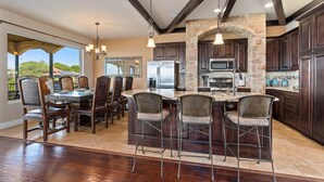 A spacious kitchen with dark wood cabinets, a stone arch, and a large island with bar stools. - Lakeview villa- spacious Mediterranean home with amazing lake views! (Canyon Lake)
