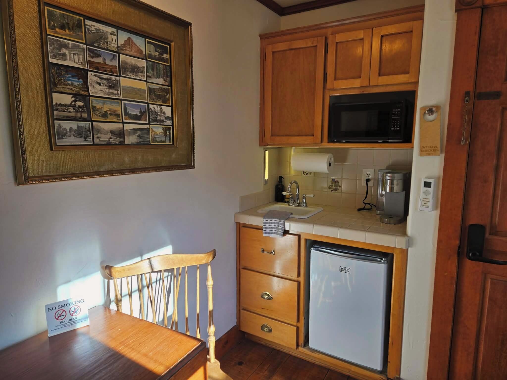 Una cocina compacta con armarios de madera, un microondas, un refrigerador y una mesa de comedor con una silla.