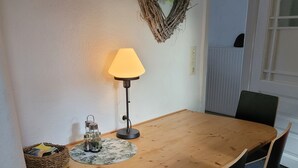 A dining table with chairs, a lamp, a basket of magazines, and a wall decoration.