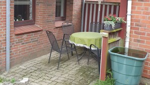 Une terrasse en briques avec une table et des chaises, une nappe verte, une plante en pot et un grand pot de fleurs vert.