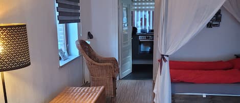 Une pièce comprenant un lit, une chaise en osier, une table et une lampe.