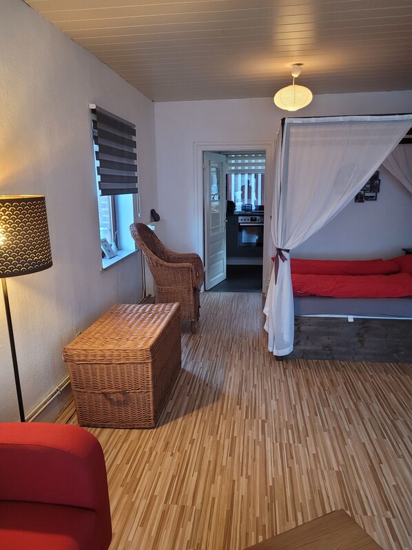 A room with a bed, a wicker chair, a table, and a lamp.