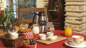 A breakfast table with a red tablecloth, a coffee pot, a clock, and a window with plants. - Gironde" guest room, swimming pool and Nordic bath (Sigalens)