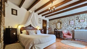 A bedroom with a large bed, wooden beams, stone walls, and a stone fireplace. - Gironde" guest room, swimming pool and Nordic bath (Sigalens)