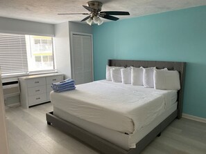 A bedroom with a bed, a ceiling fan, a window with blinds, and a white dresser. - Pool View Suite #207 (New Smyrna Beach)