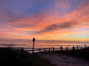 A sunset view with a wooden fence and a signpost by the beach. - Pool View Suite #207 (New Smyrna Beach)