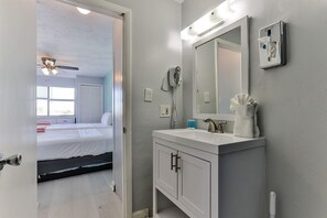 A hotel room with a bed, a bathroom with a sink and mirror, and a ceiling fan. - Pool View Suite #207 (New Smyrna Beach)