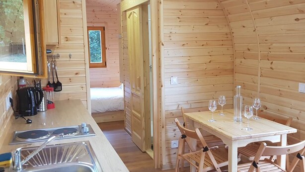 Interior acogedor de una cabaña de madera, con zona de cocina, mesa y sillas.