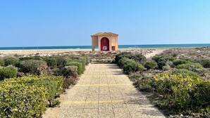 A pathway leading to a small building with a red door and a sign, surrounded by greenery and a beach in the background. - BARCARESA-LA PERLE SEA VIEW WATERFRONT AIR CONDITIONING WIFI (Port Leucate)