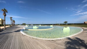 A waterfront promenade with a circular water feature, palm trees, and a clear sky. - BARCARESA-LA PERLE SEA VIEW WATERFRONT AIR CONDITIONING WIFI (Port Leucate)