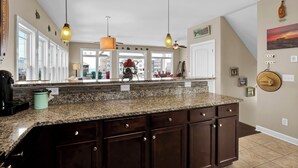 A kitchen with granite countertops, dark wooden cabinets, pendant lighting, and a view of the city through large windows. - Linens included - Amazing Views, Steps to Beach, Elevator and Fenced Yard (North Topsail Beach)