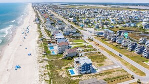 An aerial view of a coastal residential area with beachfront properties, a sandy beach, and a road running parallel to the shore. - Linens included - Amazing Views, Steps to Beach, Elevator and Fenced Yard (North Topsail Beach)