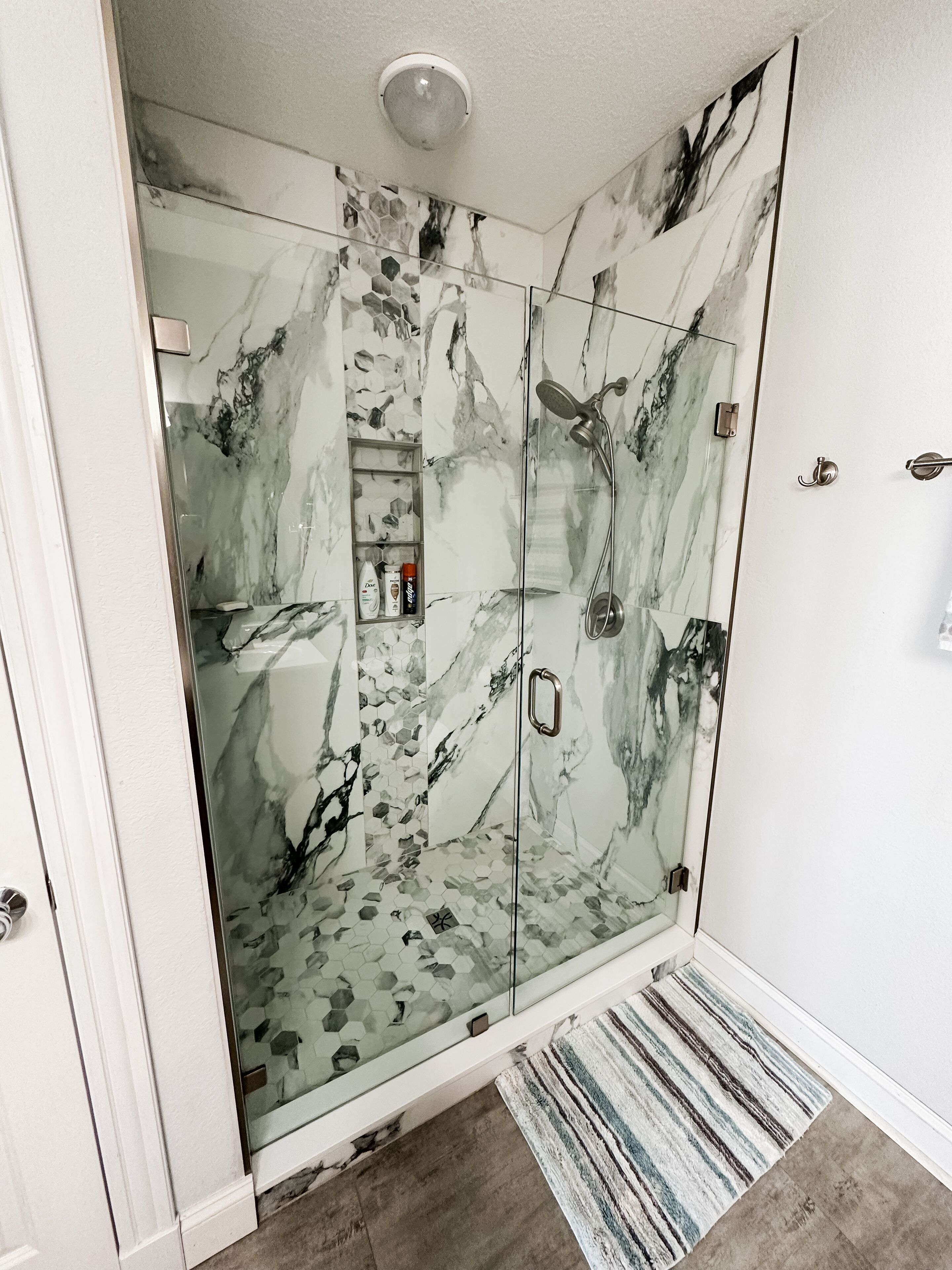 Une douche à l’italienne avec des portes en verre et un motif imitant le marbre.