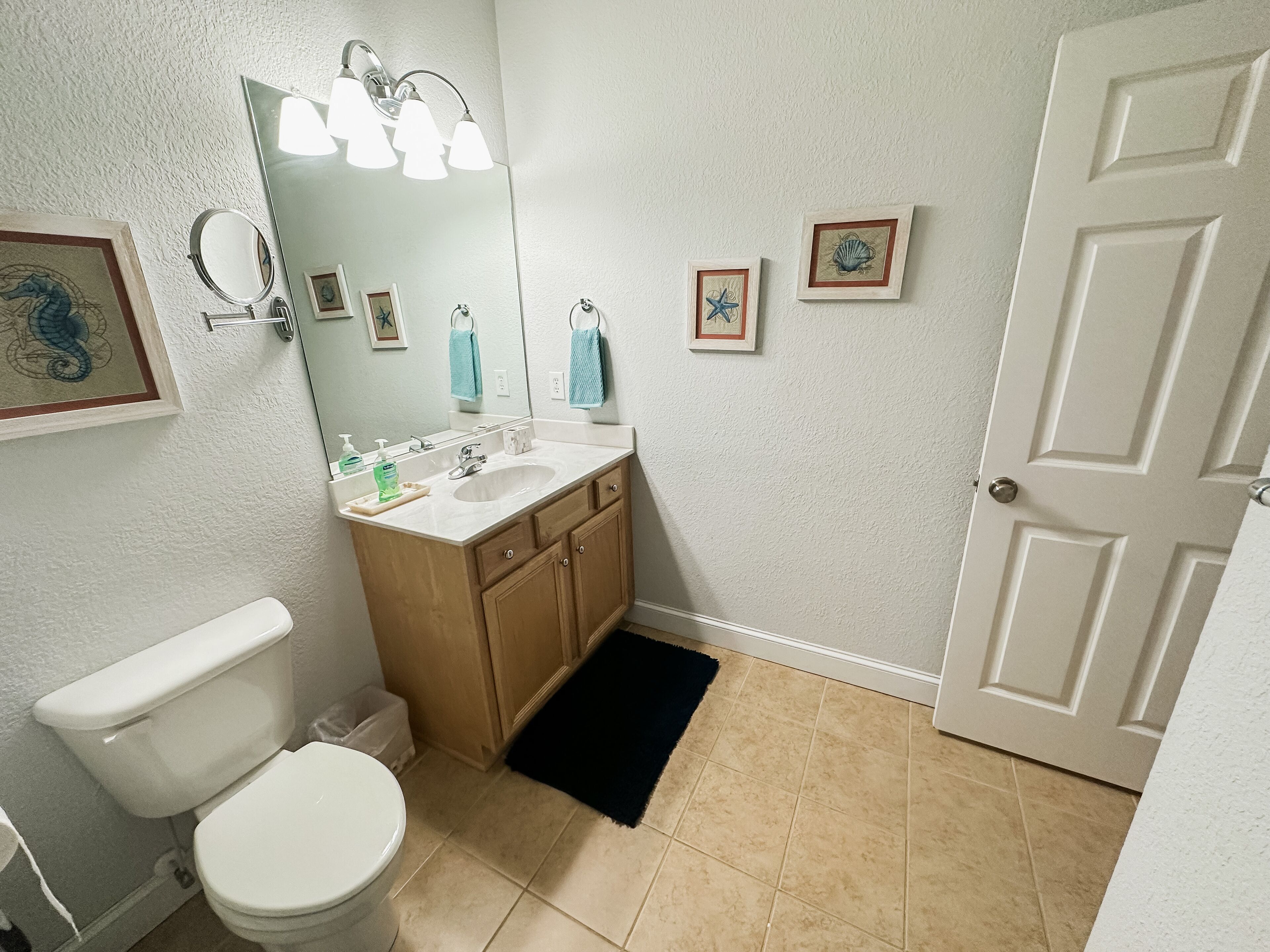Un baño con inodoro, lavabo y espejo. Se observan cuadros enmarcados en la pared y una puerta.