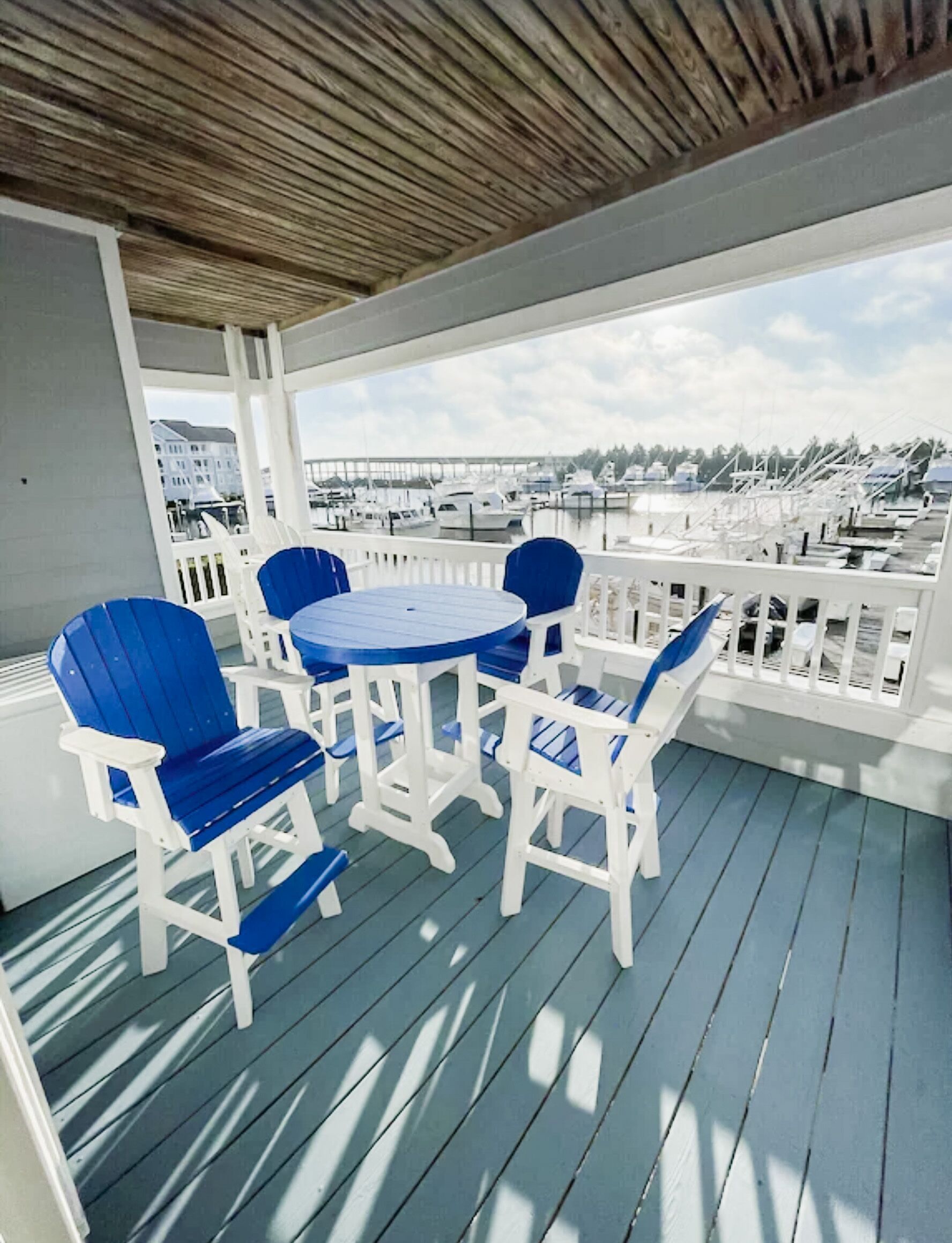 A covered outdoor seating area with a table and chairs, overlooking a marina with boats.