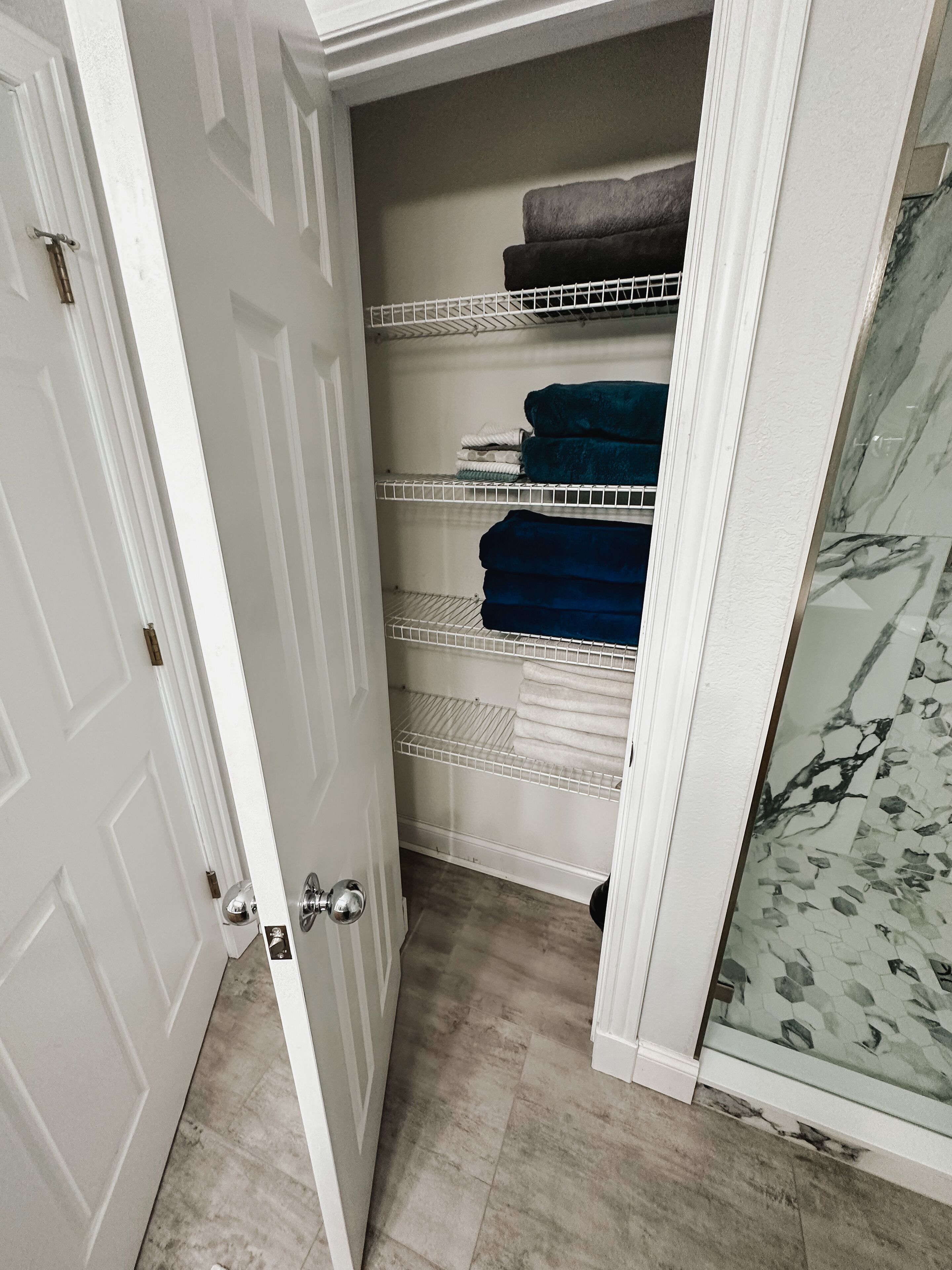 Ein begehbarer Kleiderschrank mit weißen Türen, einer Marmorablage und Regalen mit gefalteten Handtüchern.