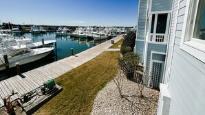 A marina with boats docked, a grassy area, and a building with a balcony. - Offshore Addiction  (Manteo)
