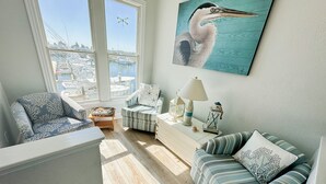 A cozy living room with a view of a marina, featuring a striped sofa, a chair, and a white side table with decorative items. - Offshore Addiction  (Manteo)