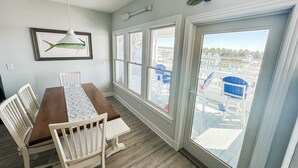 A dining area with a wooden table and chairs, a framed fish picture on the wall, and a view of a marina through large windows. - Offshore Addiction  (Manteo)