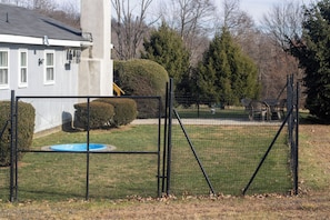 Un patio trasero cercado con piscina, una casa y un área arbolada.
