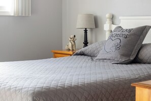 A neatly made bed with a quilted blanket, a bedside lamp, a small dog figurine, and a pillow with a dog design.