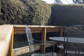 An outdoor seating area with metal chairs and a table, enclosed by a wooden fence and a hedge.