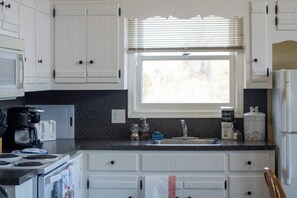 A kitchen with white cabinets, a window with blinds, a sink, and a stove.