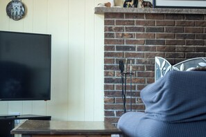 Una sala de estar con un televisor de pantalla plana, una chimenea de ladrillo y una silla metálica.