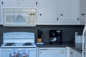 Una cocina con estufa blanca, microondas, cafetera y armarios.