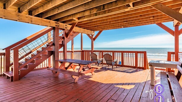 Una terraza de madera con mesas y sillas de picnic, con vista al océano.