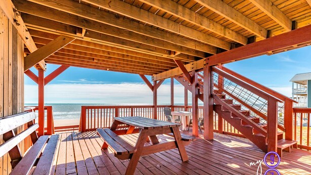Um deck de madeira com mesas de piquenique e bancos, com vista para a praia.